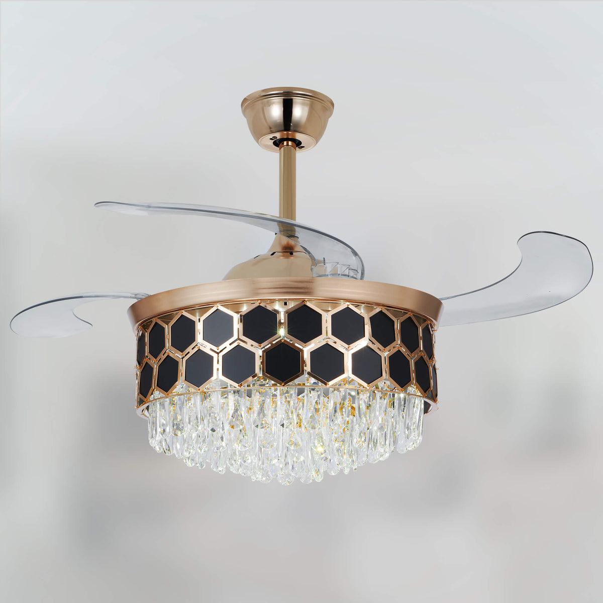A view of the gold ceiling fan, with transparent blades above its crystal chandelier light.
